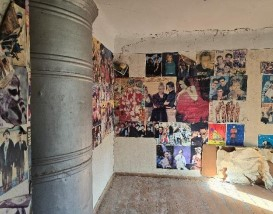 Istaba ar krāsni un uz sienām uzlīmētiem plakātiem 