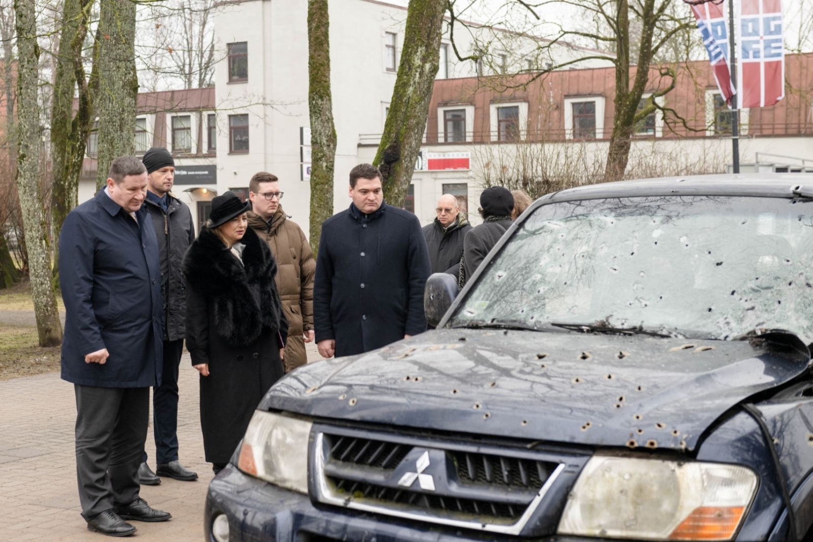 Vēstniece, domes priekšsēdētājs un citi pasākuma dalībnieki aplūko ložu cauršauto automašīnu