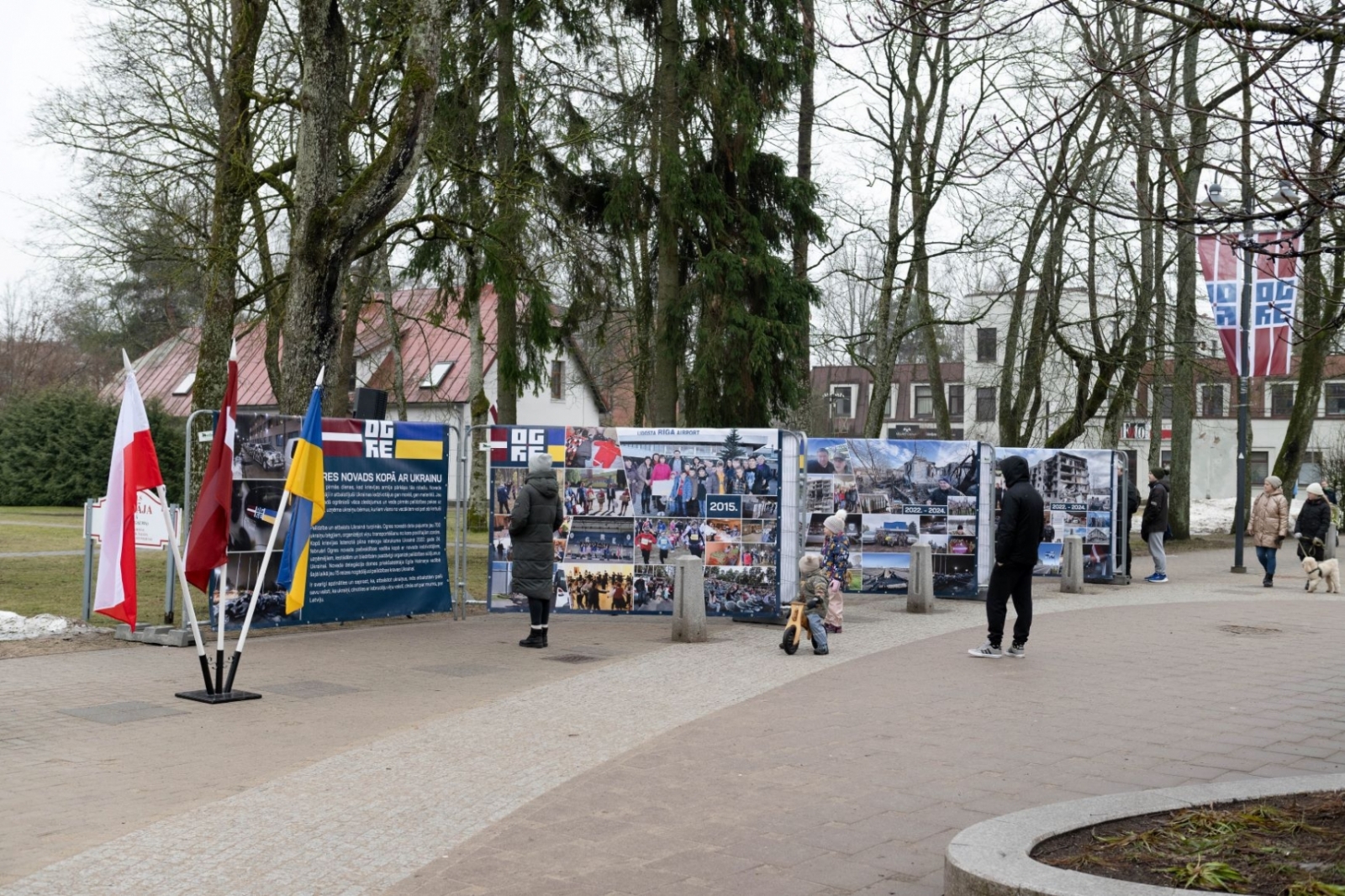 Brīvības ielā izvietotā fotoizstāde ar statīvā ievietotiem Polijas, Latvijas un Ukrainas karogiem priekšplānā
