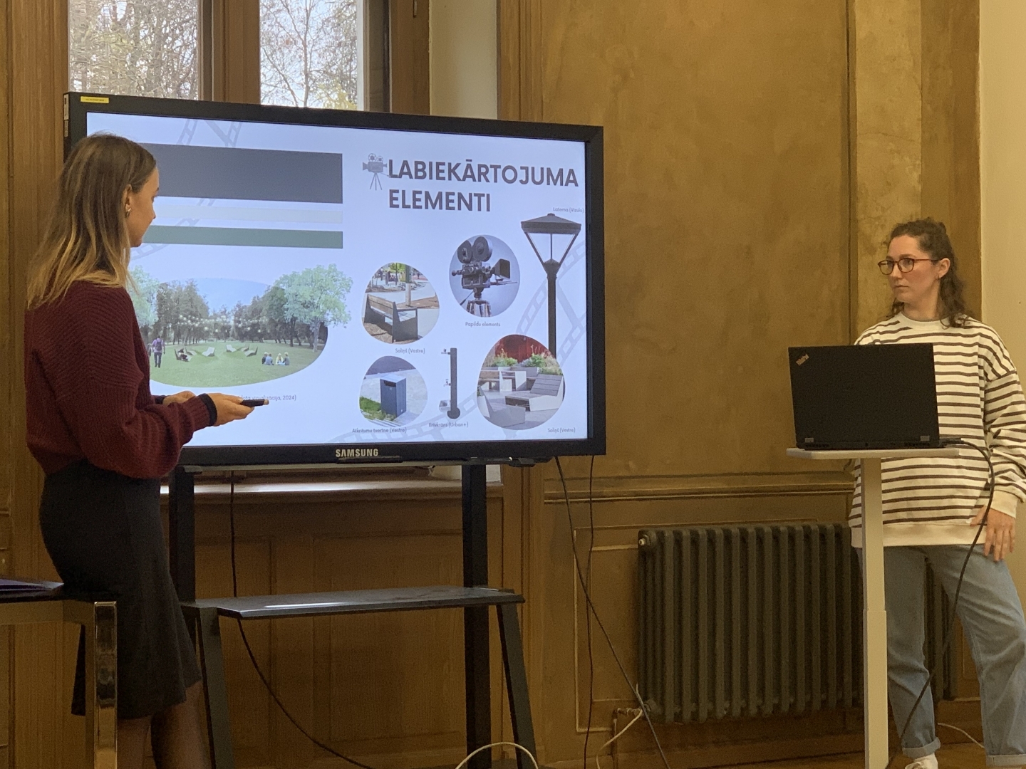 Divas studentes sniedz prezentāciju pie ekrāna
