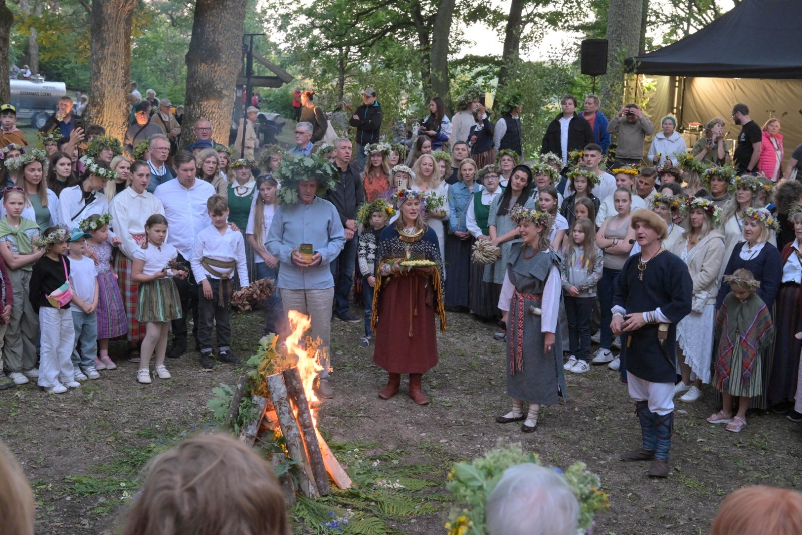 Deg Jāņu ugunskurs, apkārt stāv cilvēki Plāteres pilskalnā 20.06.2024.