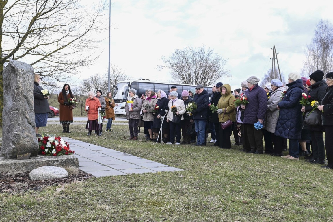 Daudzi vecāka gadagājuma cilvēki stāv pie politiski represēto piemiņas akmens Tīnūžos