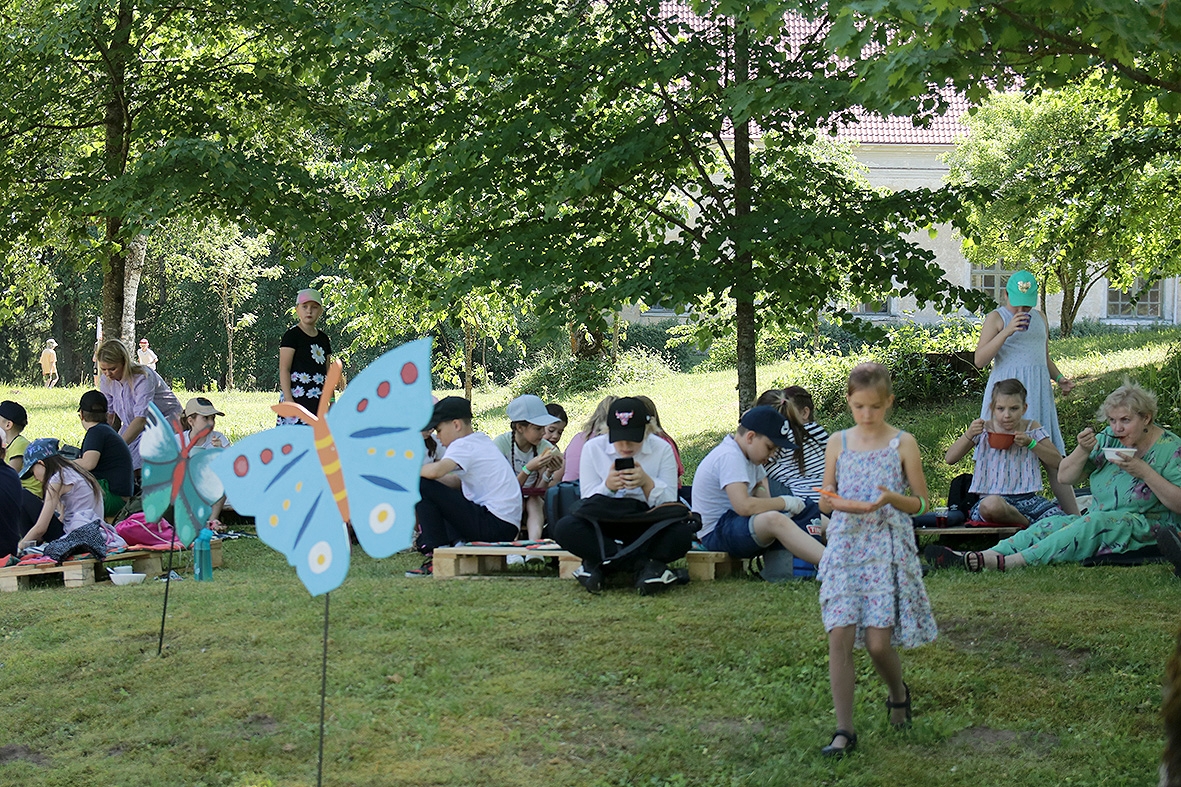 Bērni sēž pļava, rotājums taurenis  pasākumā Sadziedāsim Suntažos! 24.05.2024.