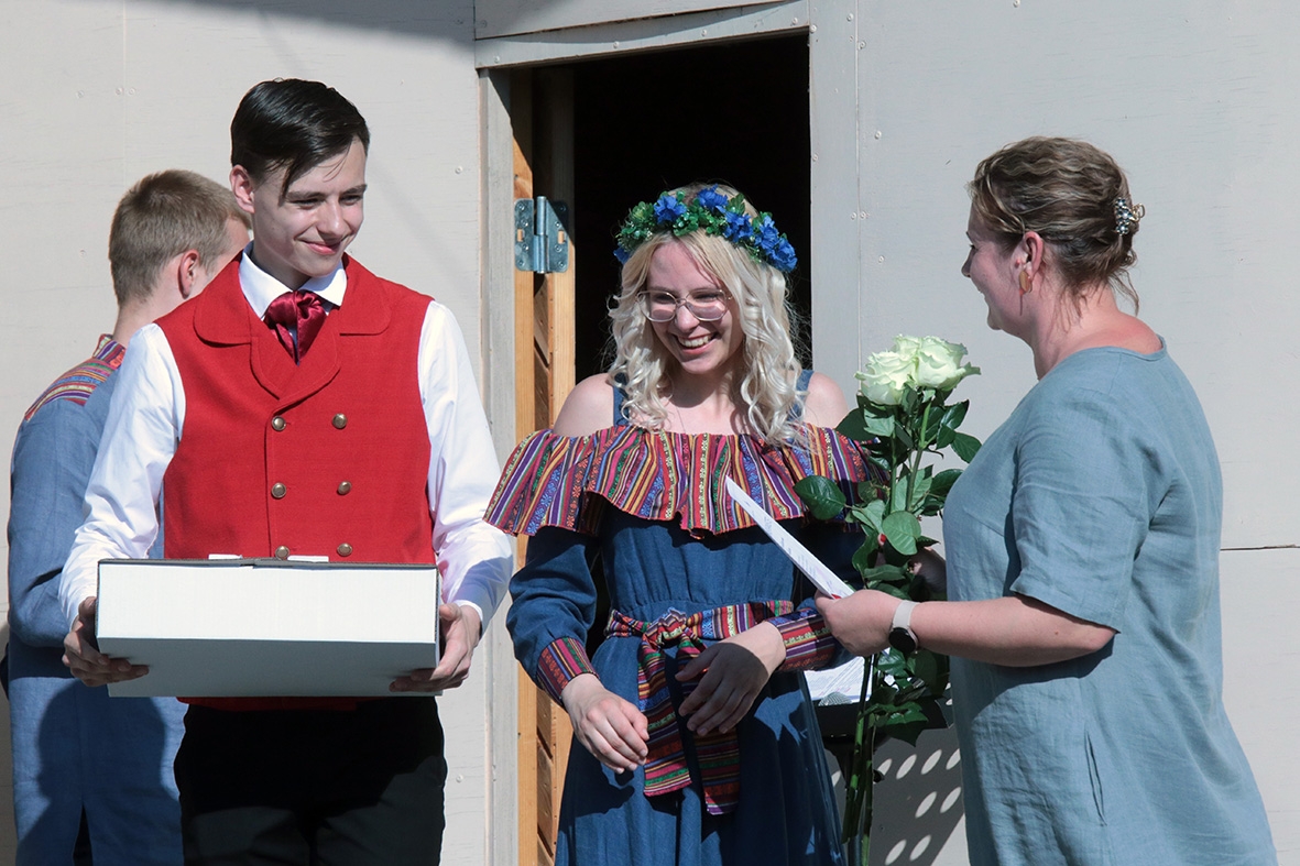 Pasniedz pateicības rakstu sievietei, zēns tur rokās kliņģeri pasākumā Sadziedāsim Suntažos! 24.05.2024.