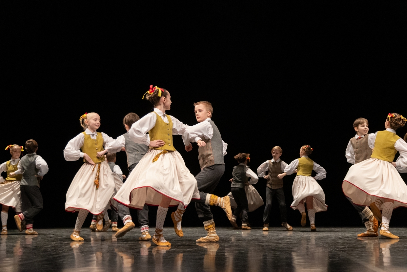 Skolēnu tautas deju skates dalībnieki uz skatuves tautas tērpos
