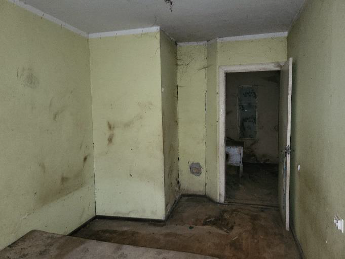 Istaba, gaiši dzeltenas, nopelējušas sienas, logs, brūna grīda, baltas durvis