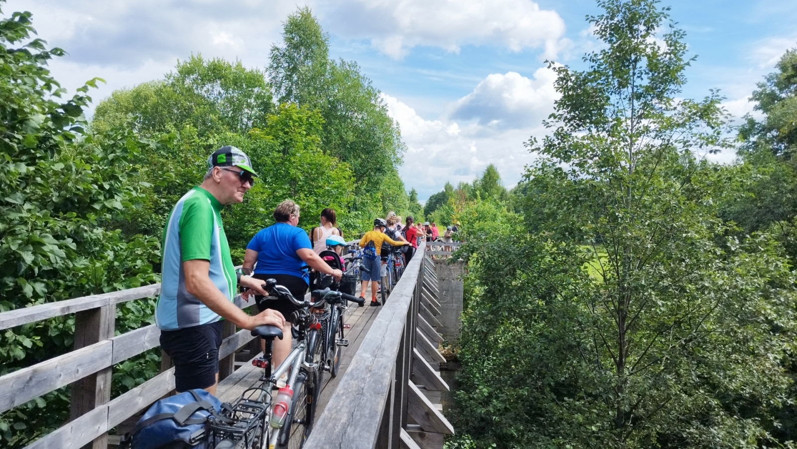 TIC organizētā velobrauciena dalībnieki Suntažu apkārtnē uz tiltiņa pār upi