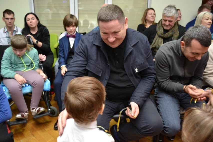 Ukrainas rehabilitācijas centrs bērniem ar īpašām vajadzībām “Atdzimšana”, bērns pasniedz dāvanu Ogres novada domes priekšsdētājam Egilam Helmanim 12.2023.