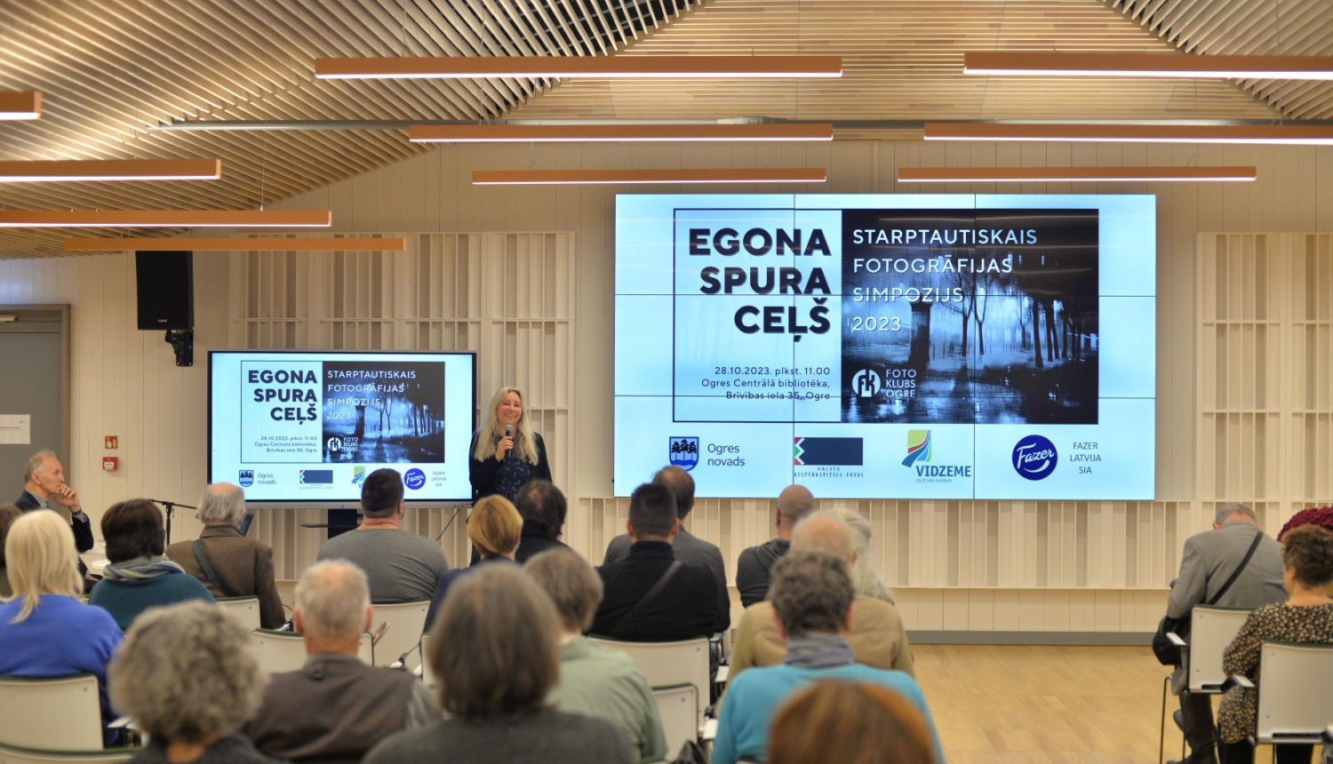 Cilvēki sēž, riekšā runā lektors Simpozijā Egona Spuras ceļš 2023. gads