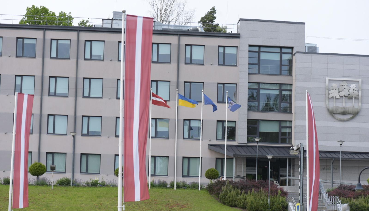 Ogres novada pašvaldības domes ēka 2025. gada pavasarī. Priekšplānā Latvijas sarkanbaltsarkanie karogi