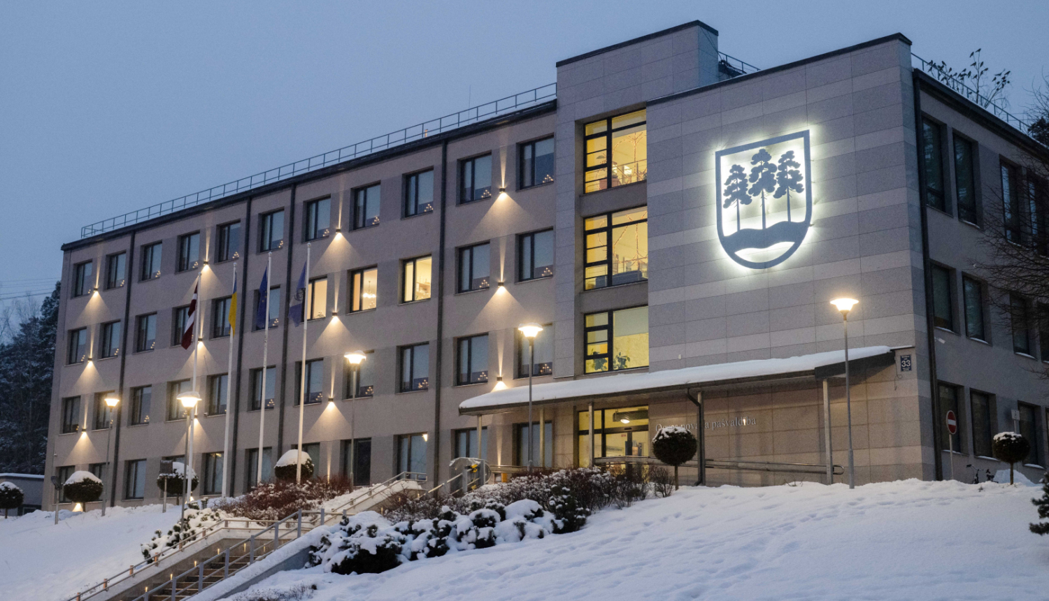 Ogres novada pašvaldības domes ēka ziemā, izgaismota krēslas stundā.