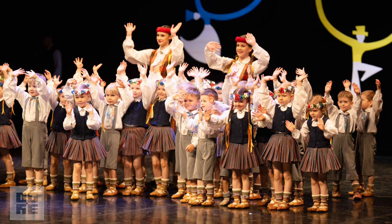 Bērnu deju kolektīva "Spolītes" dalībnieki, stāvot uz Tautas nama skatuves, māj ar rokām skatītājiem