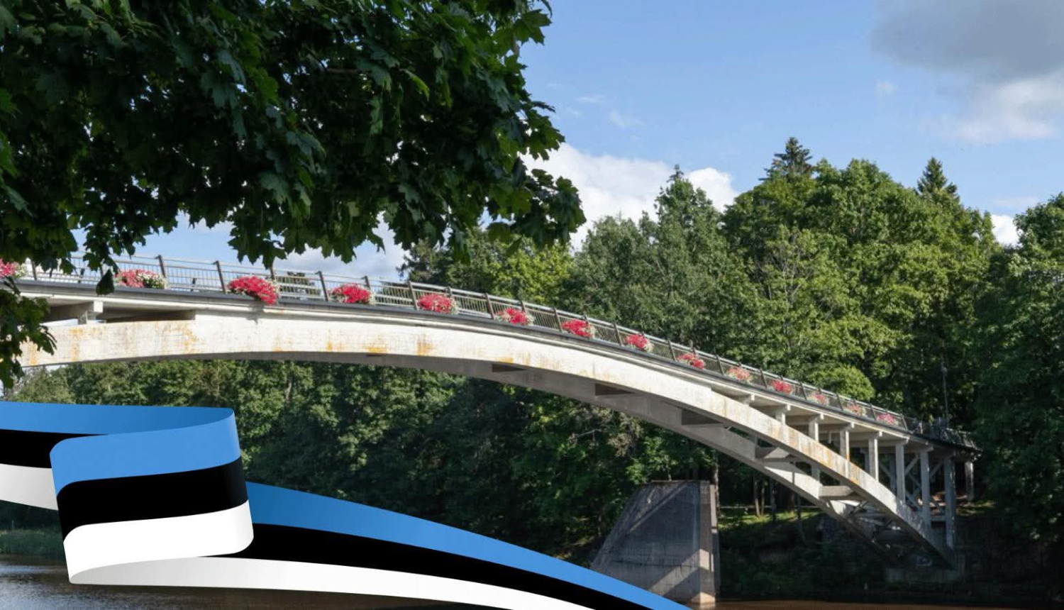 Lokveida tilts pār Ogres upi ar ziedu kastēm un lenti Igaunijas karoga krāsās attēla priekšplānā 