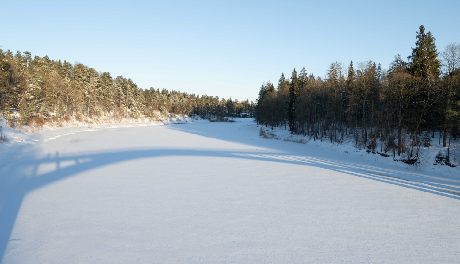 Ogres upe ziemā, ēnā uz ledus atspīd gājēju tilts