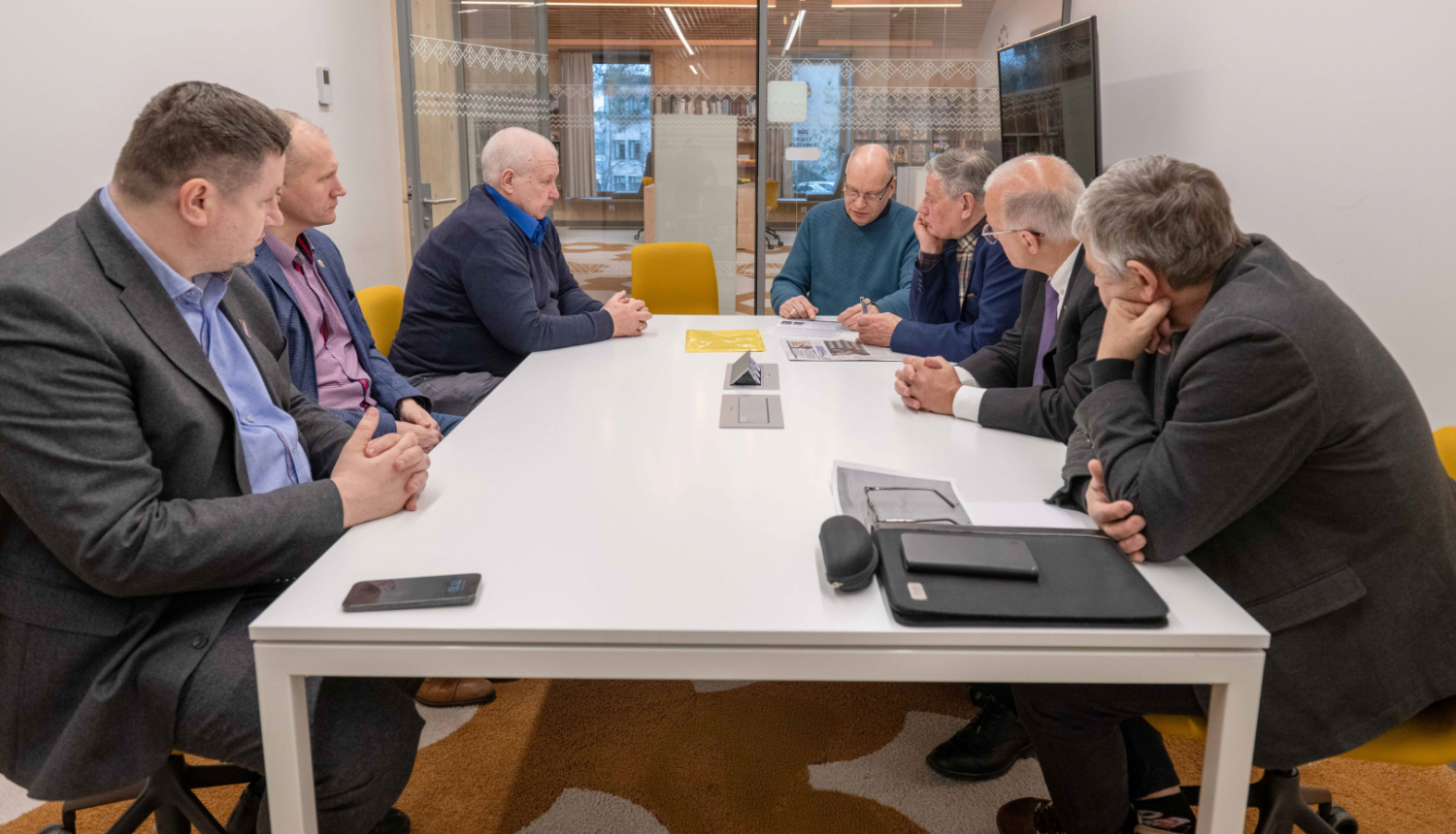 Tikšanās dalībnieki pie apspriežu galda klausās vēsturnieka stāstījumu