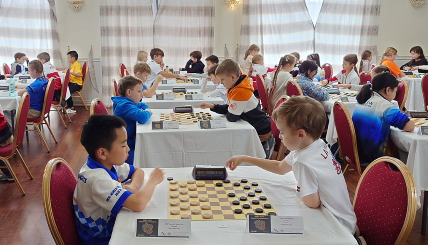 Sacensības dambretē Polijā, spēlē divi zēni. 11.2023.