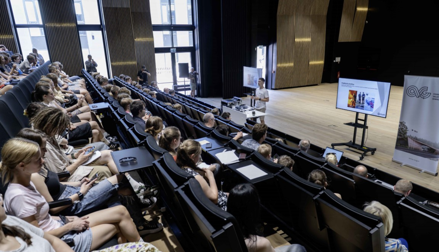 Jaunieši Ogres Valsts ģimnāzijas aulā skatās prezentāciju 28.05.2024.