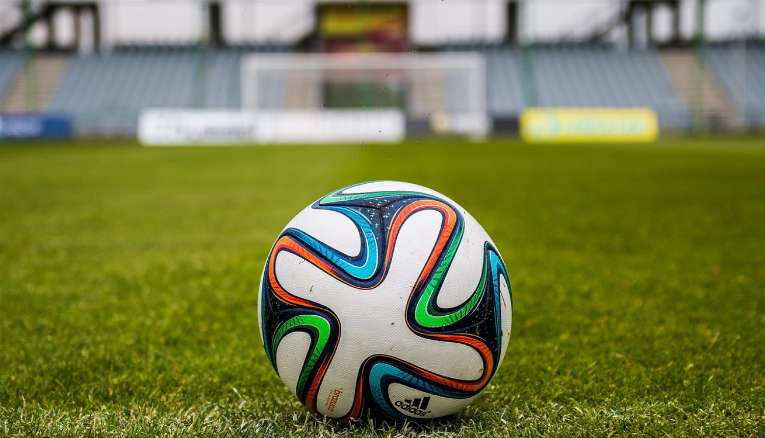 Futbola bumba stadionā ar mākslīgās zāles segumu zaļā krāsā. Fonā tribīnes.