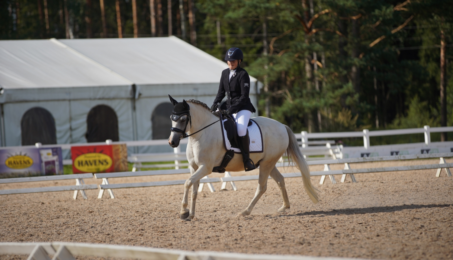 Meitene tumšā tērpā jāj uz zirga 08.2024.