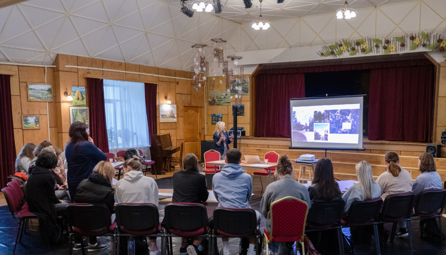 Ķeipenes tautas namā studenti sēž pie galda, fonā prezentācija 11.09.2024.
