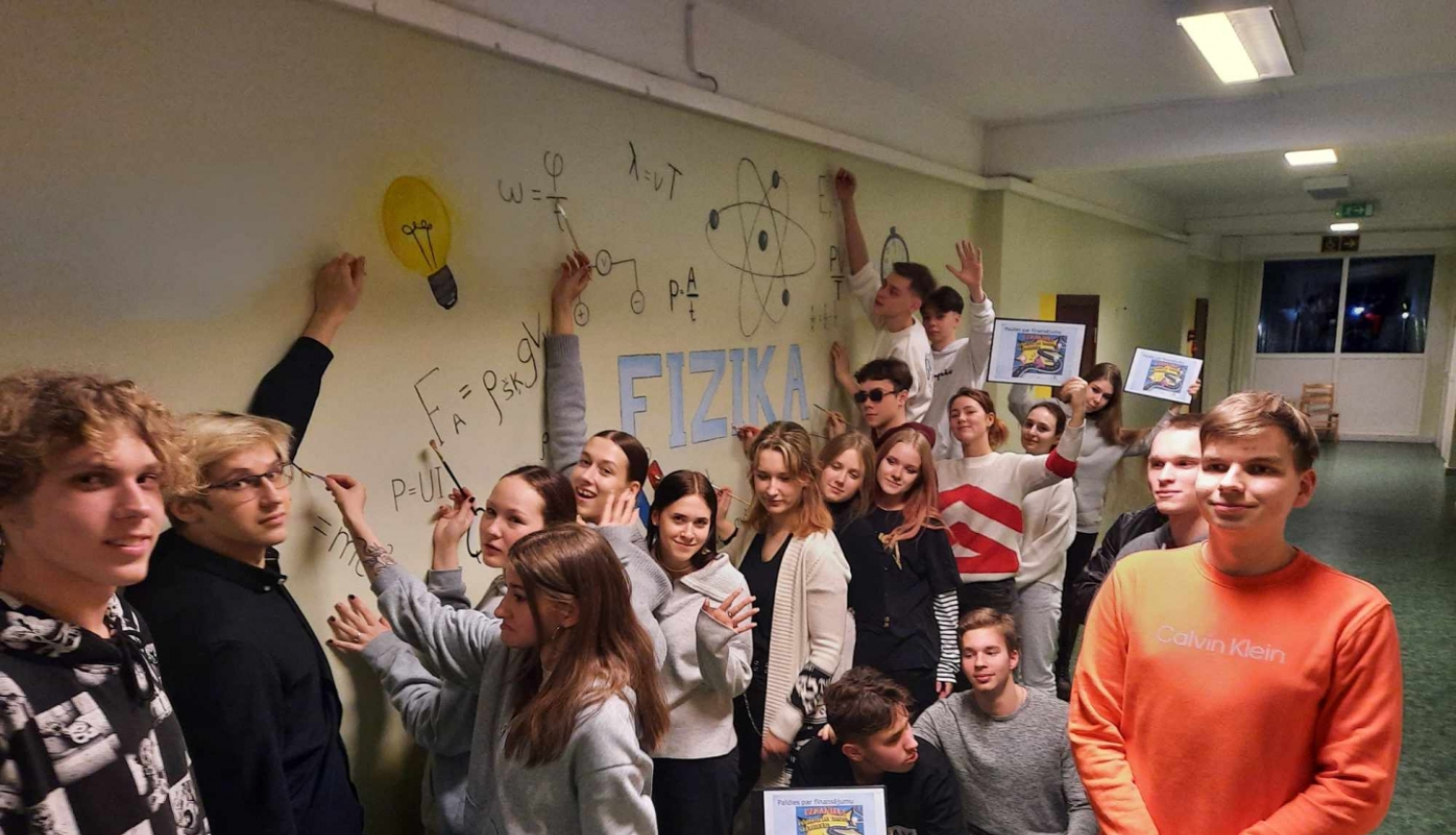 Aptuveni 20 jaunieši pie izveidotās fizikas likumu sienas