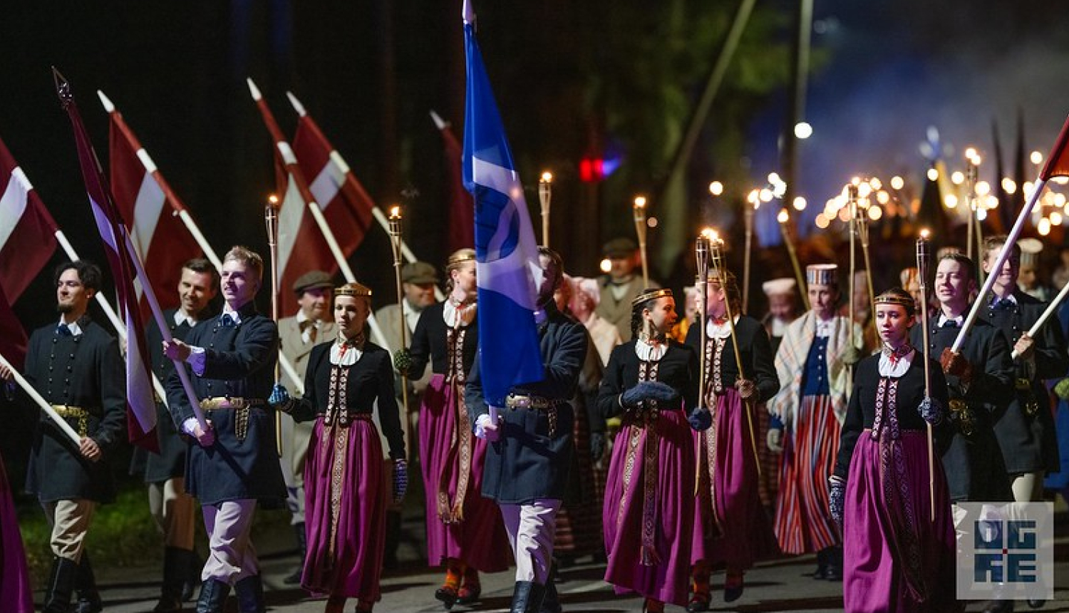 Lāpu gājiens Ogrē par godu Lāčplēša dienai. Priekšplānā jaunieši tautas tērpos, rokās nesot Ogres karogu un Latvijas karogus