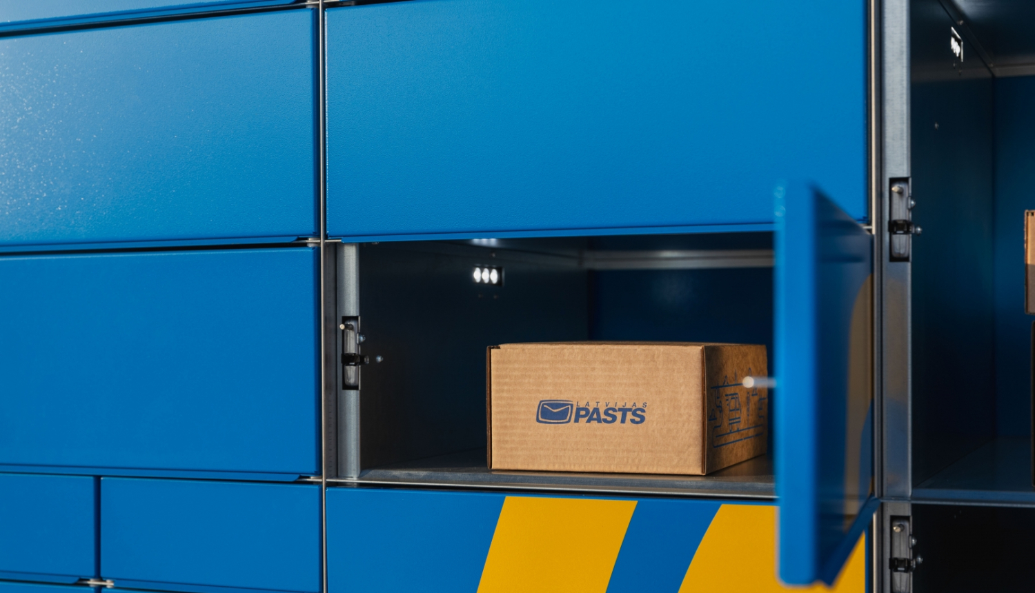 Latvijas pasta pakomāts ar atvērtām nodalījuma durtiņām un ievietotu kartona kasti