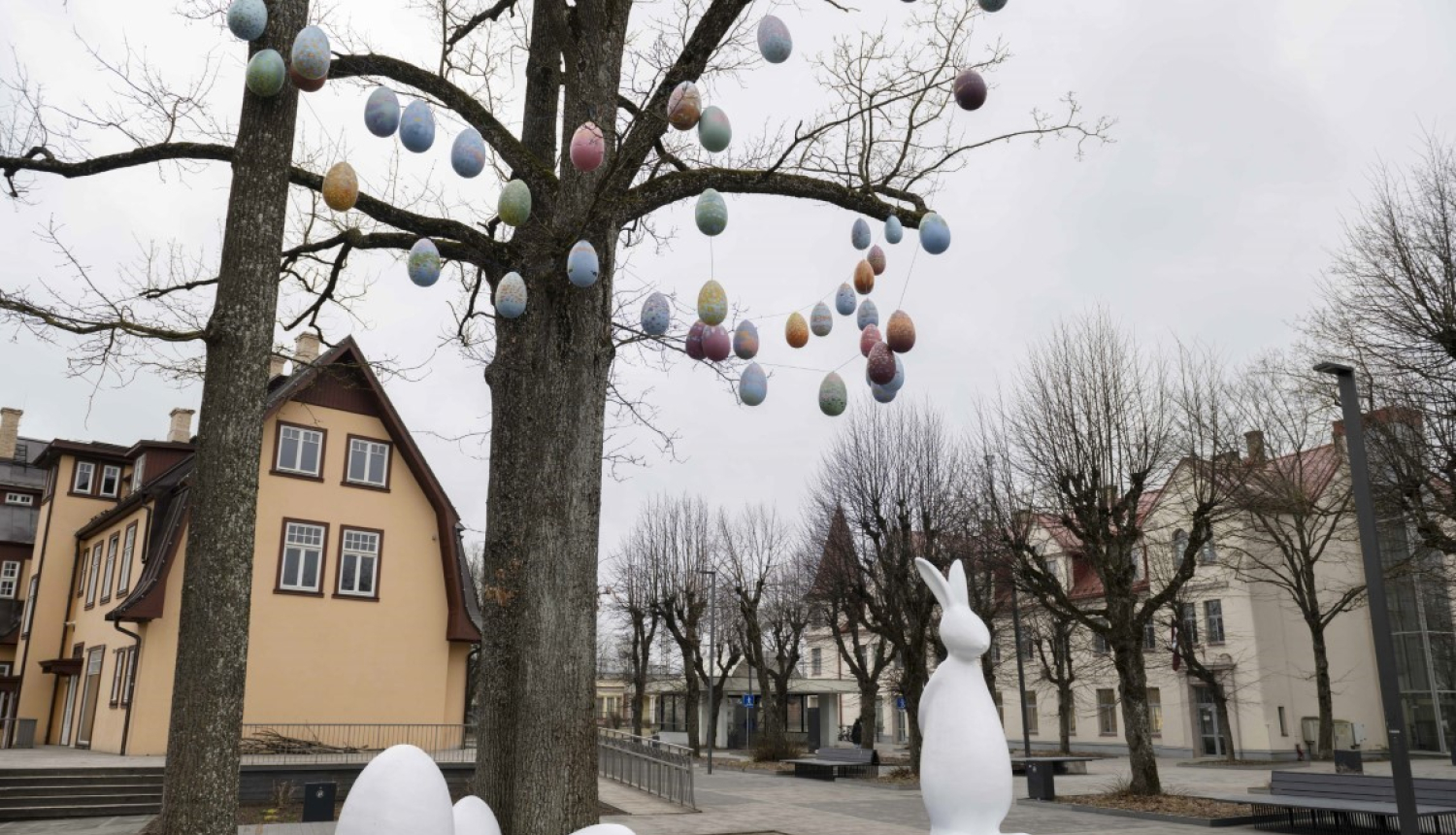 Balts Lieldienu zaķis ar olām pie koka, zaros iekārtas mazas olas