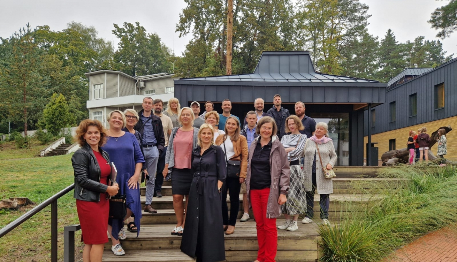 Pasākuma dalībnieki stāv uz Ogres Centrālās bibliotēkas kāpnēm