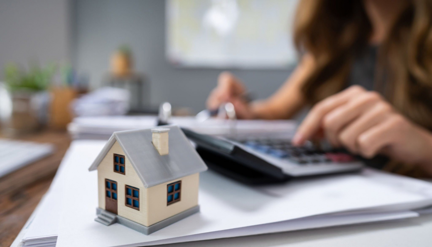 Kartona māja, fonā sieviete ar kalkulatoru