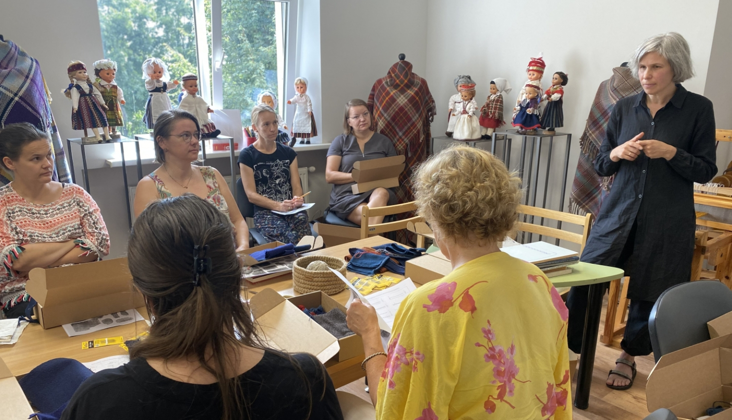 Nodarbību dalībnieces sēž ap galdu un klausās nodarbību vadītājas teikto