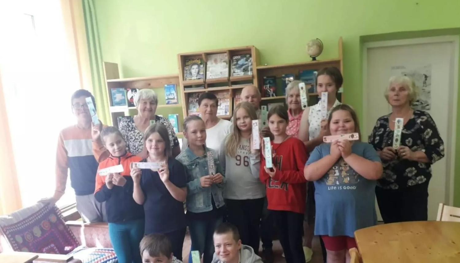 Seniori ar jauniešiem stāv ar dažādiem pašu veidotiem priekšmetiem rokās 08.2024.