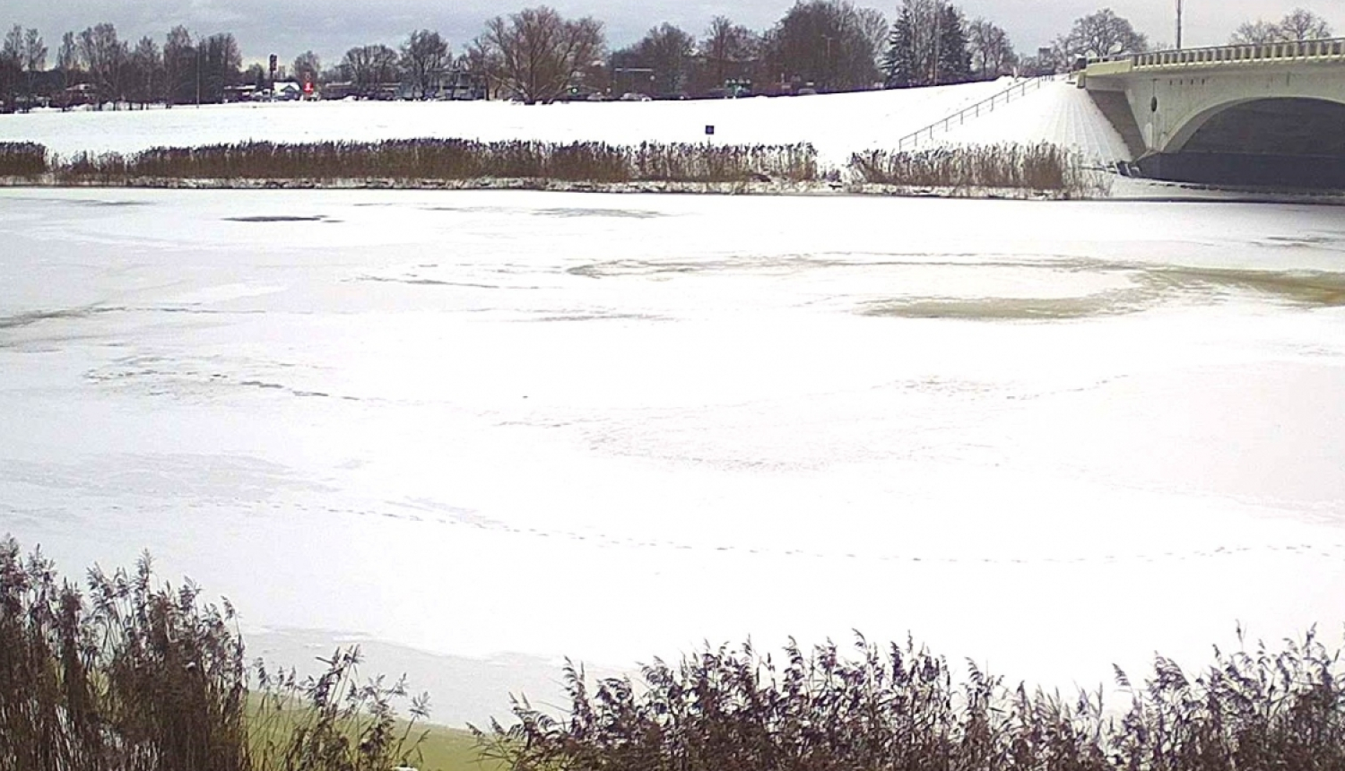 Upe noklāta ar ledu, fonā tilts