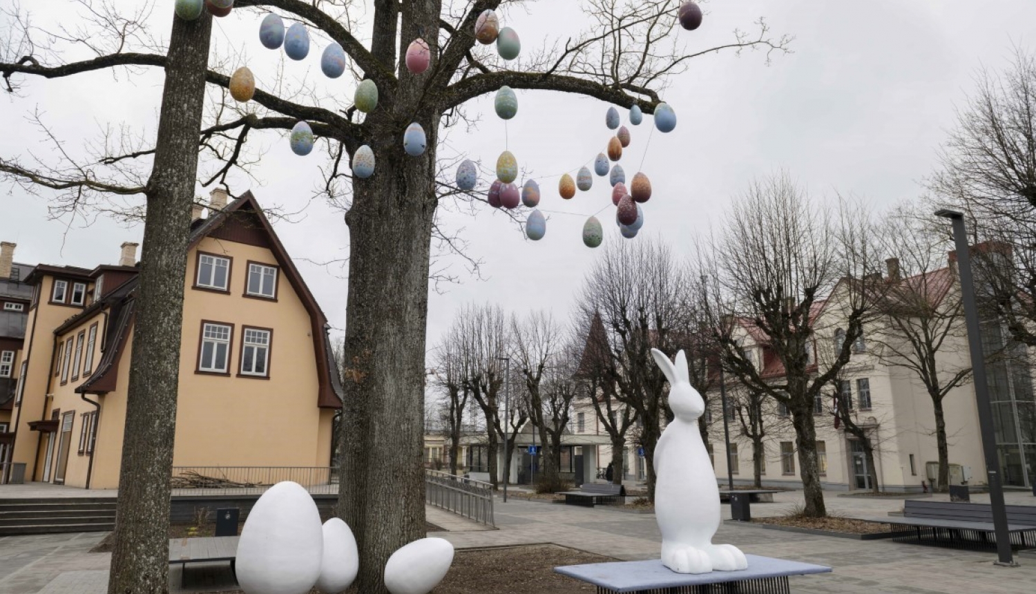 Balts Lieldienu zaķis ar olām pie koka, zaros iekārtas mazas olas