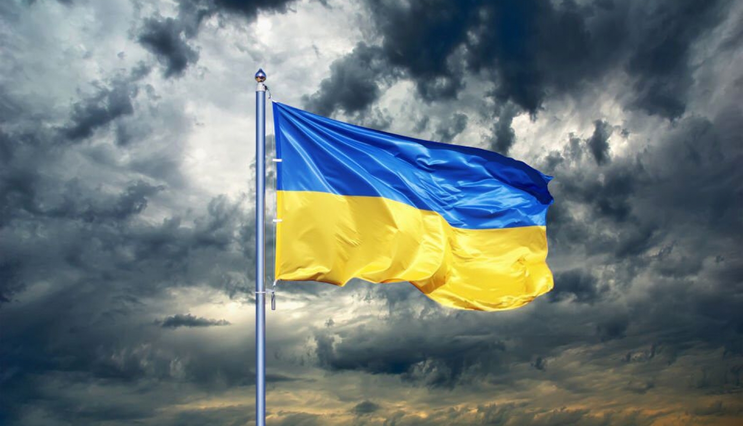 Vējā plīvojošs Ukrainas karogs uz mākoņainu debesu fona