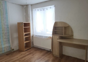 Istaba ar gaišas krāsas sienām, logu un dažām koka mēbelēm
